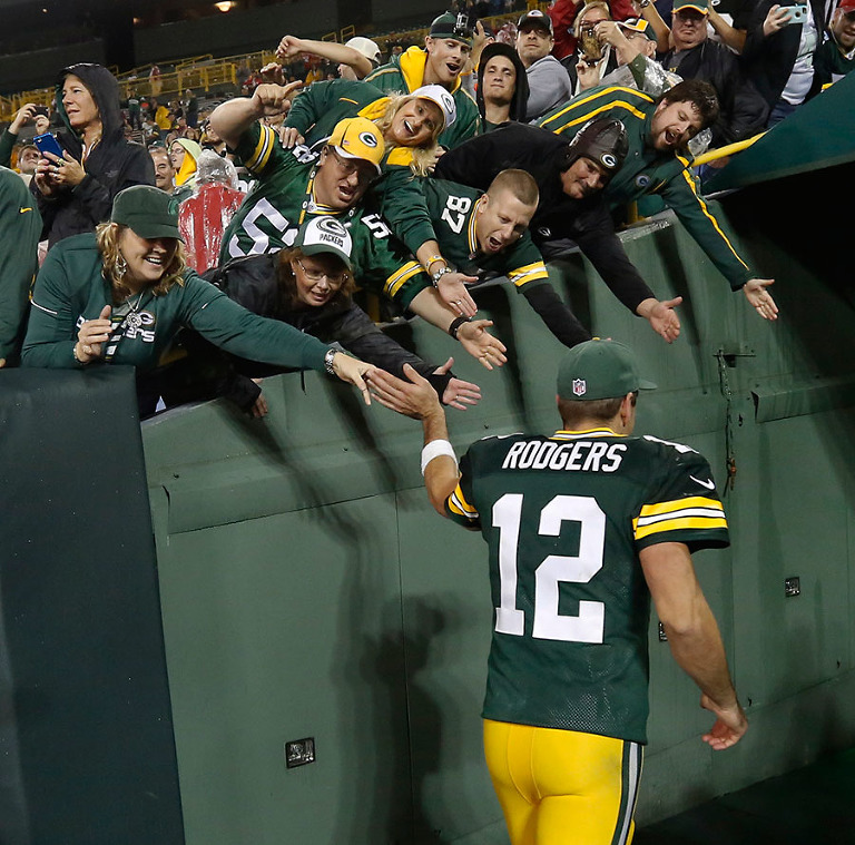 Green Bay Packers quarterback Aaron Rodgers celebrates with fans as he walks off the field.